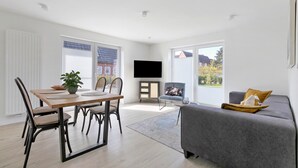 Una sala de estar moderna con una mesa de comedor, sillas, un sofá, un televisor de pantalla plana y ventanas amplias.