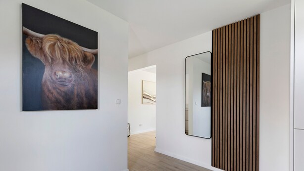 Un interior moderno con un cuadro grande de una vaca, un espejo y un panel de pared de madera.
