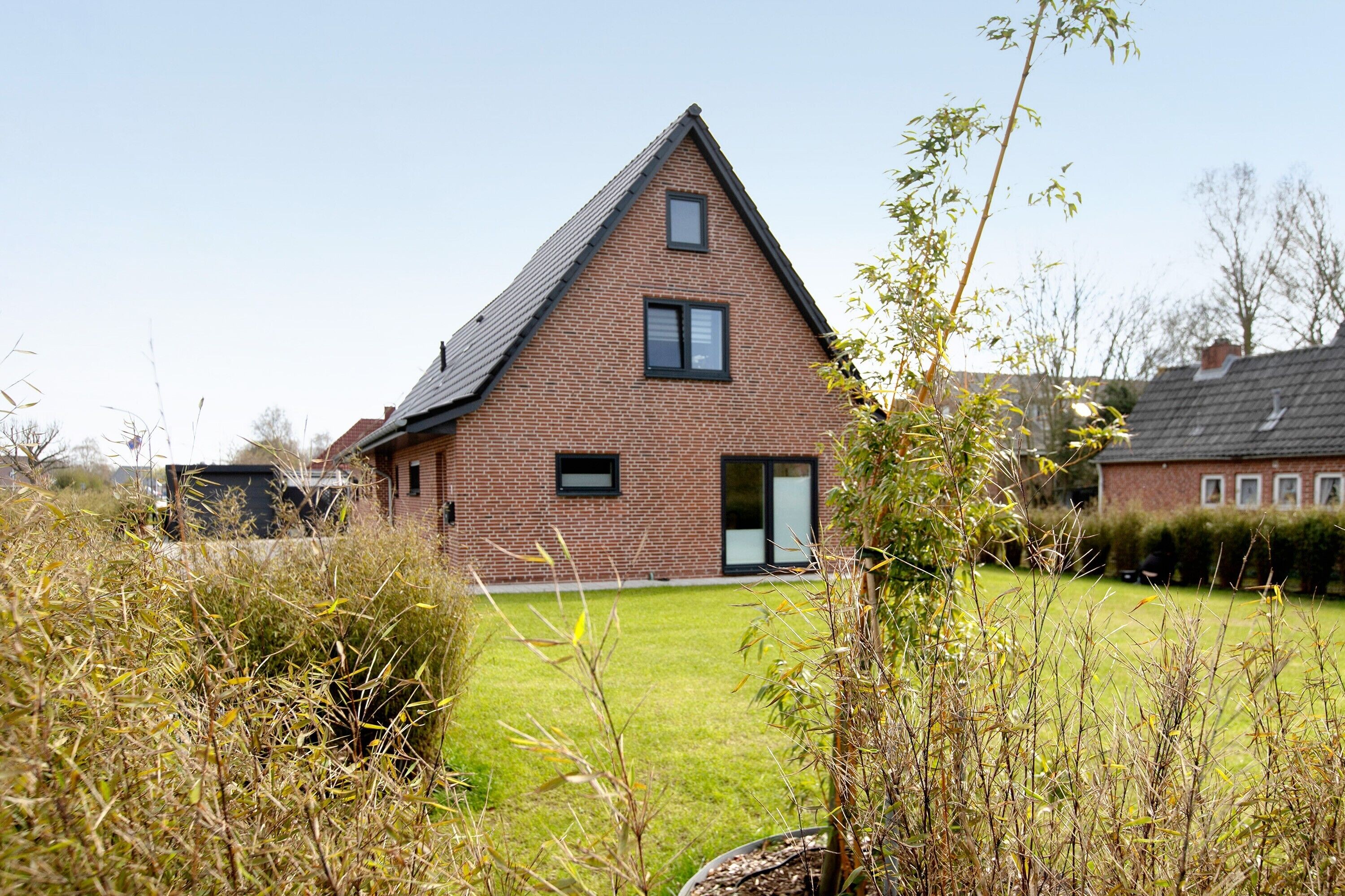 A single-story brick house with a sloped roof, a front door, and a small front yard with grass and shrubs.