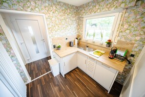 Une cuisine avec des plans de travail en bois, des meubles blancs, une fenêtre ornée de plantes et une porte.