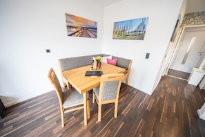 Un coin repas avec une table et des chaises en bois, un banc et deux tableaux accrochés au mur.