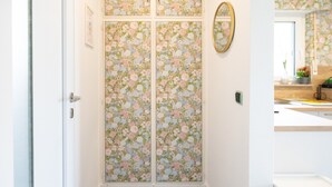 Passadís amb terres de fusta, una porta a l'esquerra i una paret amb paper pintat floral.