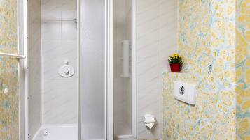 Une douche avec une porte en verre, des toilettes avec un abattant en bois et un mur recouvert de carreaux décoratifs.