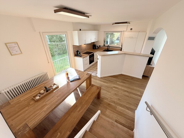 Eine moderne Küche mit weißen Schränken, einem Holztisch und Blick ins Freie.