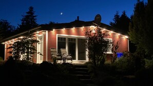Een huis met een schotelantenne, een overdekte patio met stoelen en een zichtbare maan aan de hemel.