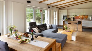 Een moderne woonkamer met een bank, een houten salontafel en een eettafel gedekt met eten en drinken.