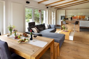 A modern living room with a sofa, wooden coffee table, and a dining table set with food and drinks.