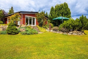 Une maison rouge avec un mur en pierre, une pelouse verte et un grand arbre.