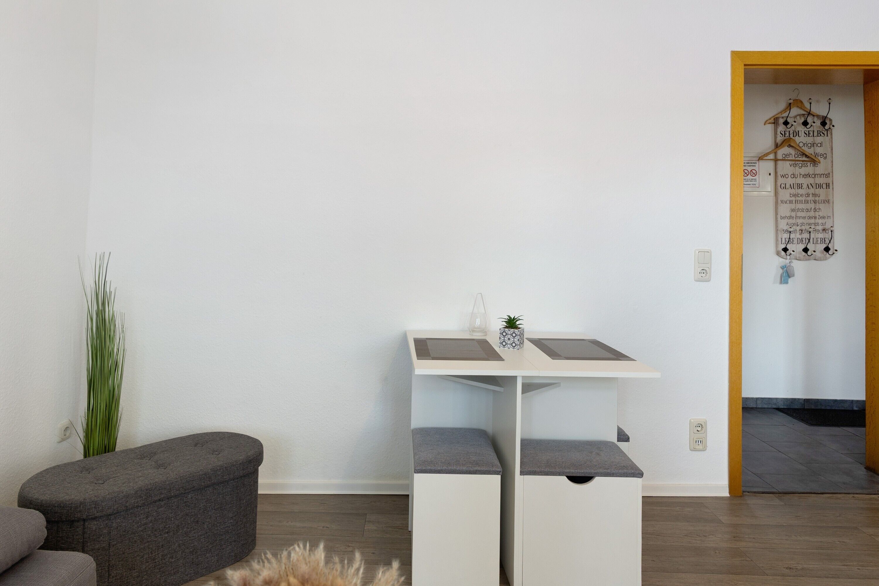 A modern room with a white desk, grey cushions, a small plant, and a wooden door with a sign.