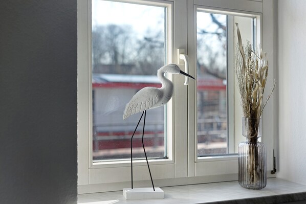A white bird sculpture on a stand by a window with a vase of dried plants. - Holiday Apartment "Havelvorland" with Shared Terrace and Wi-Fi (Havelberg)