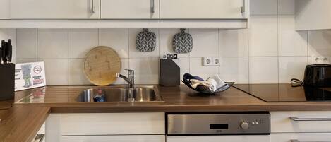 A modern kitchen with white cabinets, a stainless steel sink, a wooden countertop, and a built-in dishwasher.