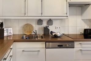 A modern kitchen with white cabinets, a stainless steel sink, a wooden countertop, and a built-in dishwasher.