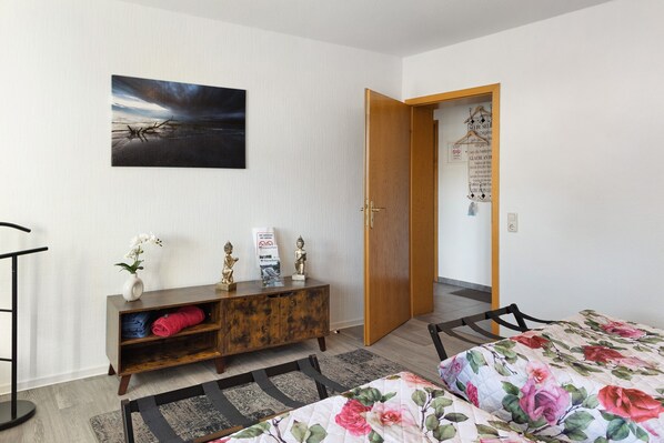 A bedroom with a bed, a wooden cabinet, a painting, and a door leading to another room.