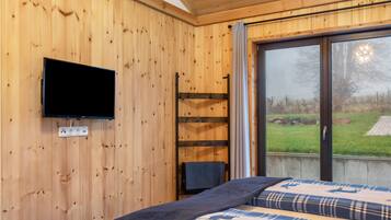 A wooden-paneled room with a bed, a television mounted on the wall, and a window with a view of the outdoors.