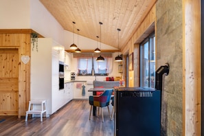 Una cocina moderna con detalles de madera, iluminación colgante, un comedor con sillas coloridas y un ventanal amplio.