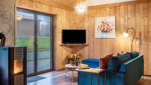 A modern living room with a flat-screen TV, a blue sofa, a fireplace, and wooden walls.