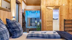 A wooden interior with a bed, pillows, and a view of a stone wall and a window.
