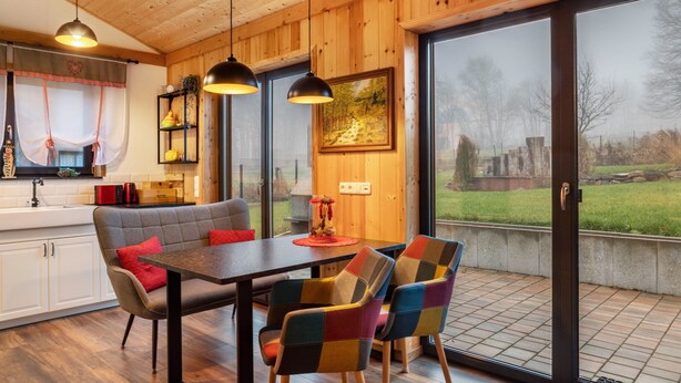 A wooden interior with a dining area, kitchen, and large sliding glass doors to a garden.