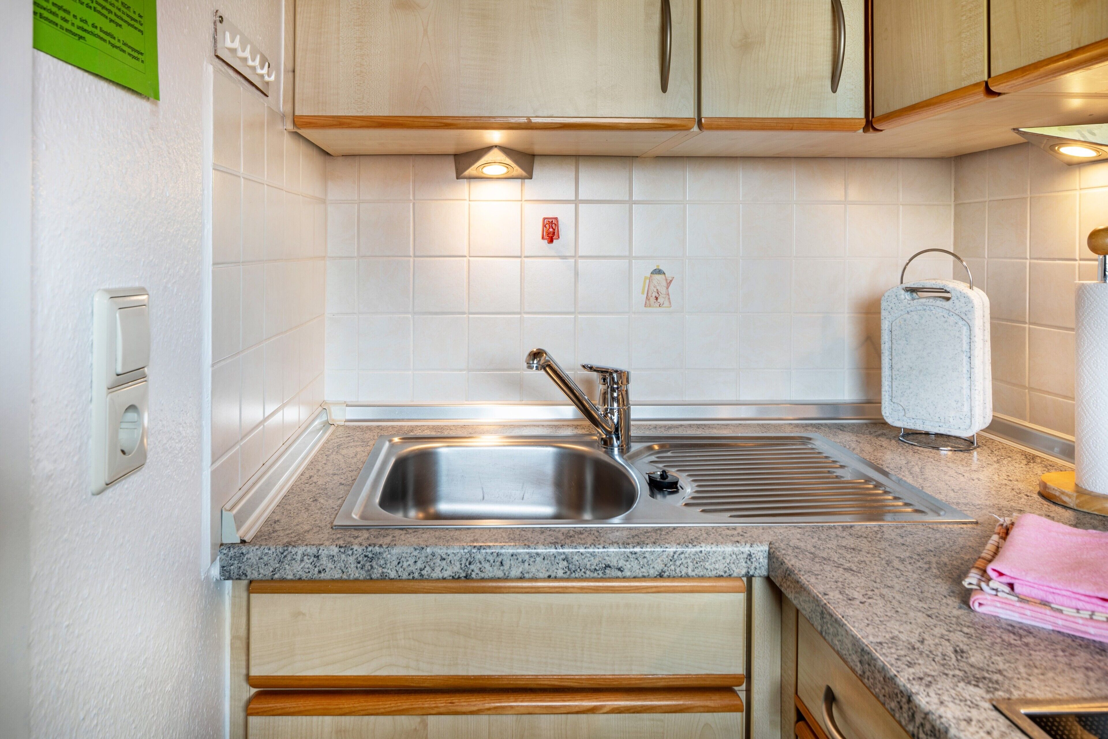 A kitchen with a stainless steel sink, wooden cabinets, a granite countertop, and a paper towel dispenser.
