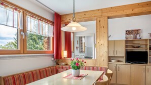 Un espace repas comprenant une table en bois, des bancs, une plante en pot et des armoires en bois.