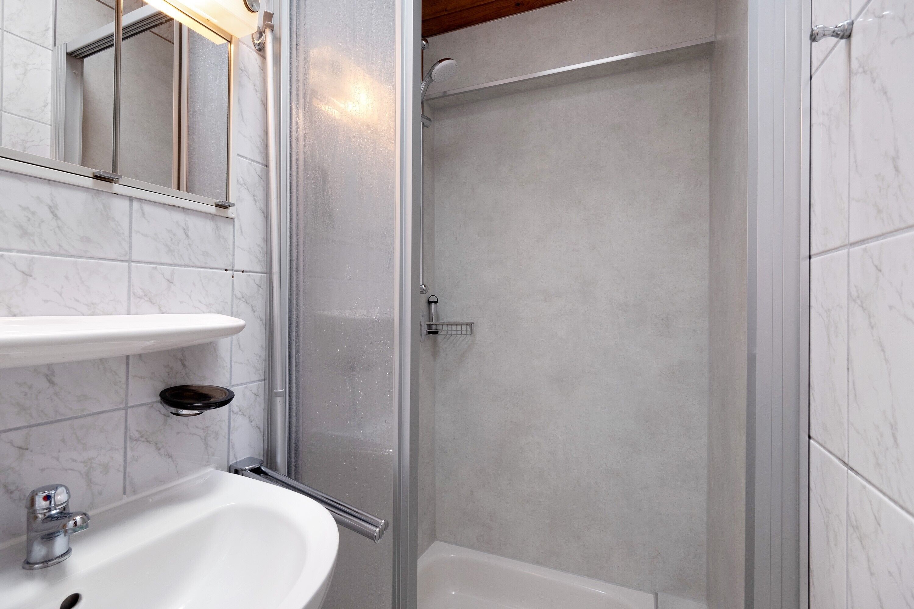 A bathroom with a white sink, mirror, and shower enclosure.