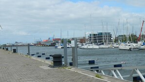 Un port de plaisance avec des bateaux amarrés, une promenade pavée et des bâtiments industriels en arrière-plan.