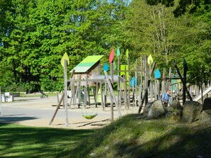 Un terrain de jeux doté de diverses installations, notamment un toboggan et des balançoires, le tout entouré d’arbres.