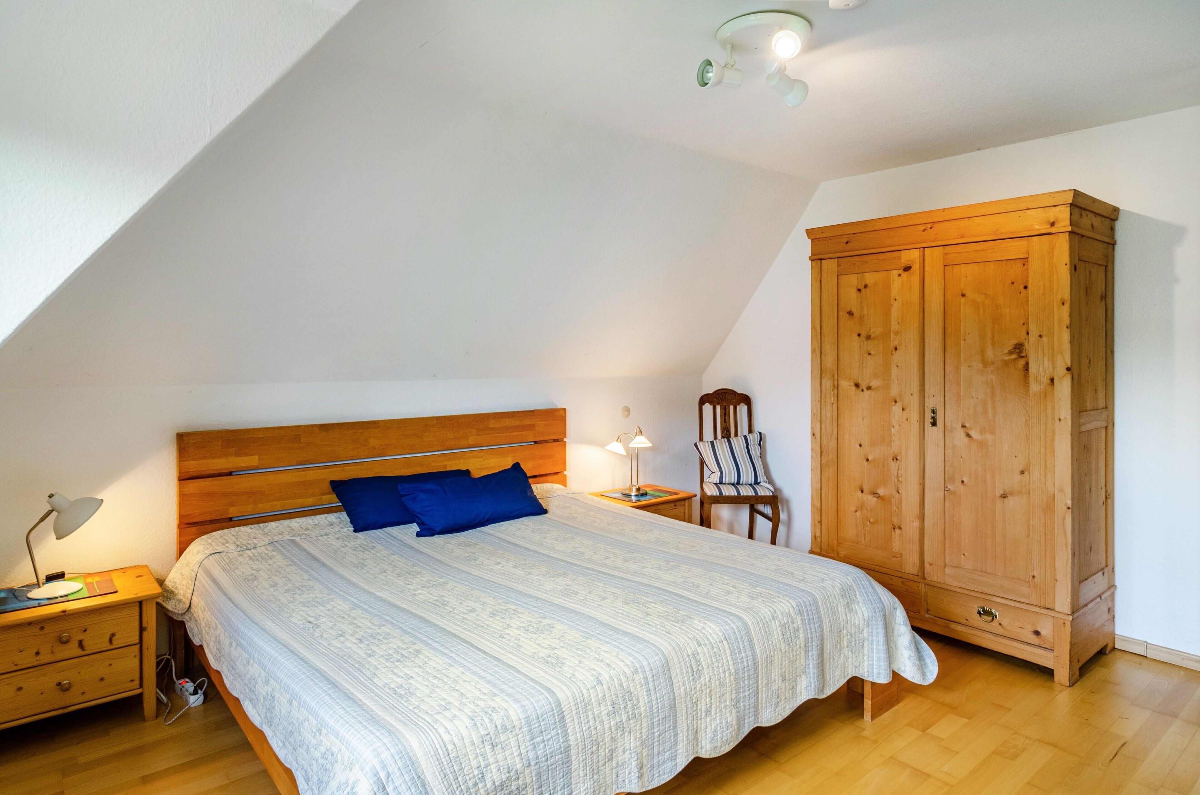A bedroom with a wooden bed, a nightstand, a chair, a wardrobe, and a sloped ceiling.
