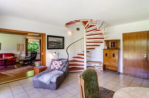A living room with a spiral staircase, a red sofa, a grey sofa, a wooden cabinet, and a large mirror.