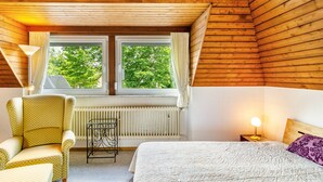 Une pièce confortable avec un lit, une chaise, une table et une fenêtre avec des rideaux.