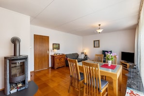 En stue med brændeovn, sofa, spisebord med stole, fjernsyn og pejs.