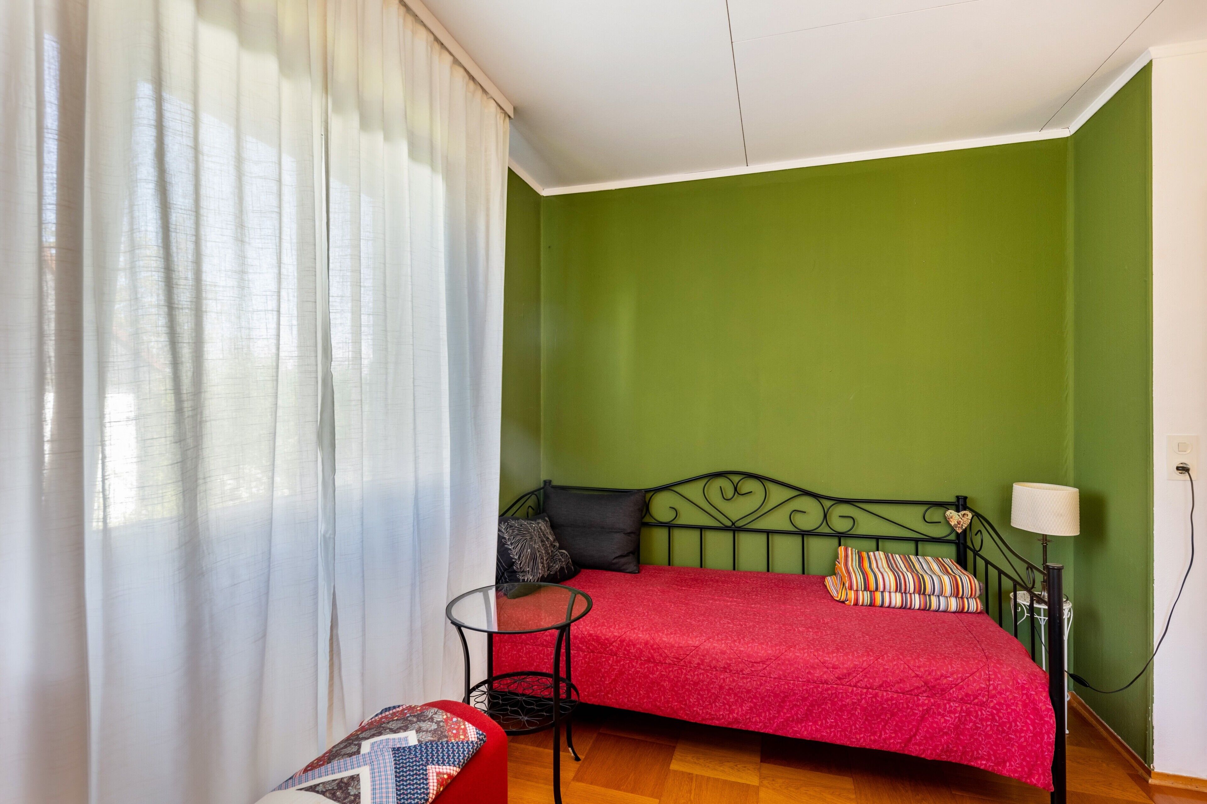 Una habitación con cama, una mesita, una lámpara y un ventanal con cortinas.