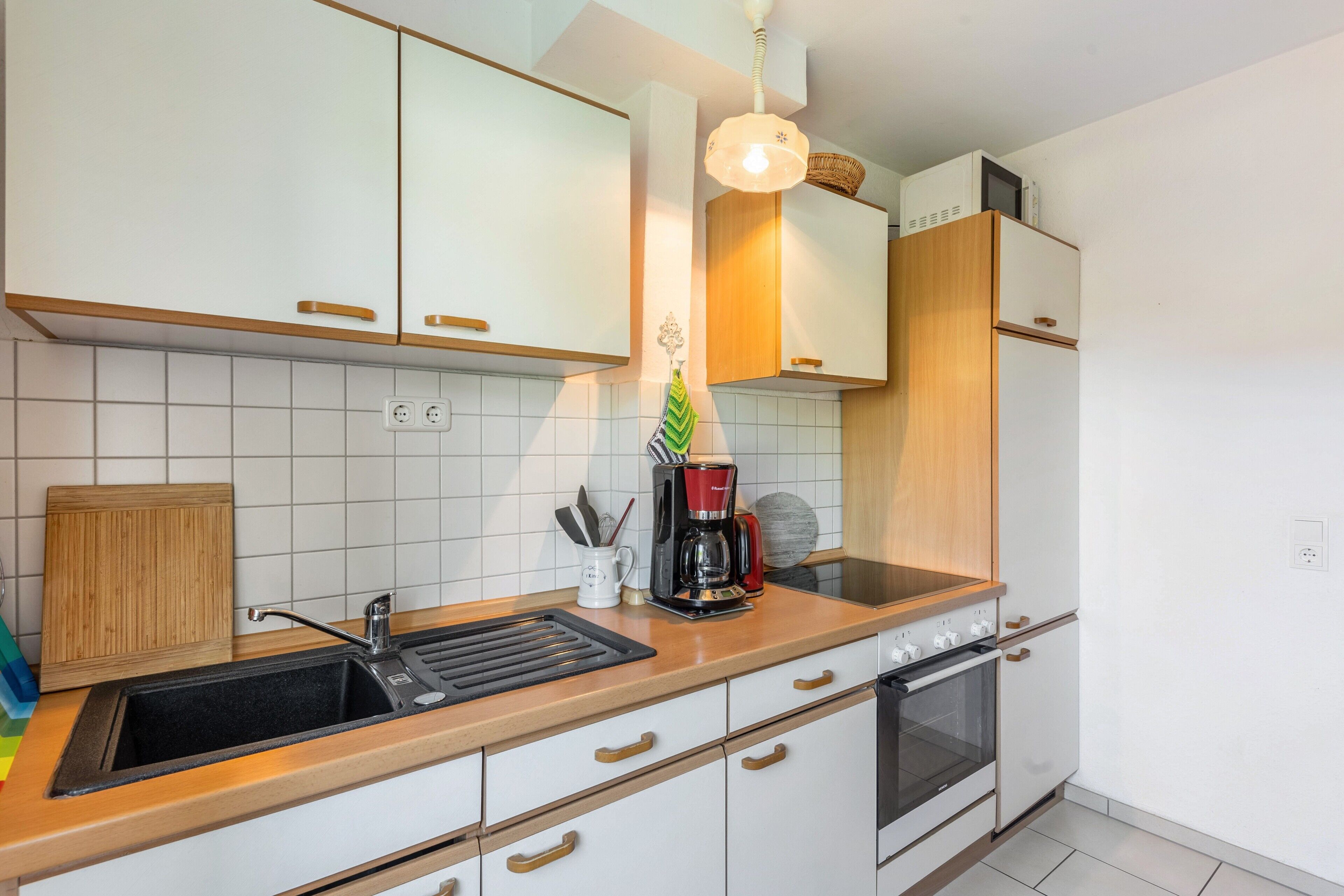 A modern kitchen with white cabinets, a black sink, a coffee maker, and a built-in oven.