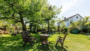 Un patio con una mesa y sillas, un árbol grande y una casa al fondo.