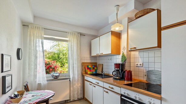 Una cocina con armarios blancos, encimera de madera, estufa y ventana con vista a zonas verdes.