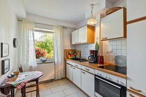 Ett kök med vita skåp, en bänkskiva i trä, en spis och ett fönster med utsikt över grönområden.