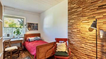A bedroom with a wooden bed, a desk, a chair, a window with a view, and a wall with a wooden pattern.