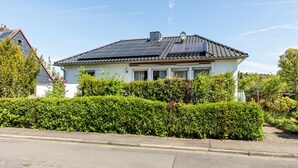 Una casa con paneles solares, fachada blanca y un seto cuidado.