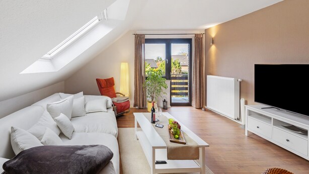 Un salon moderne comprenant un canapé, une table basse, un téléviseur et une porte-fenêtre coulissante donnant sur un balcon.