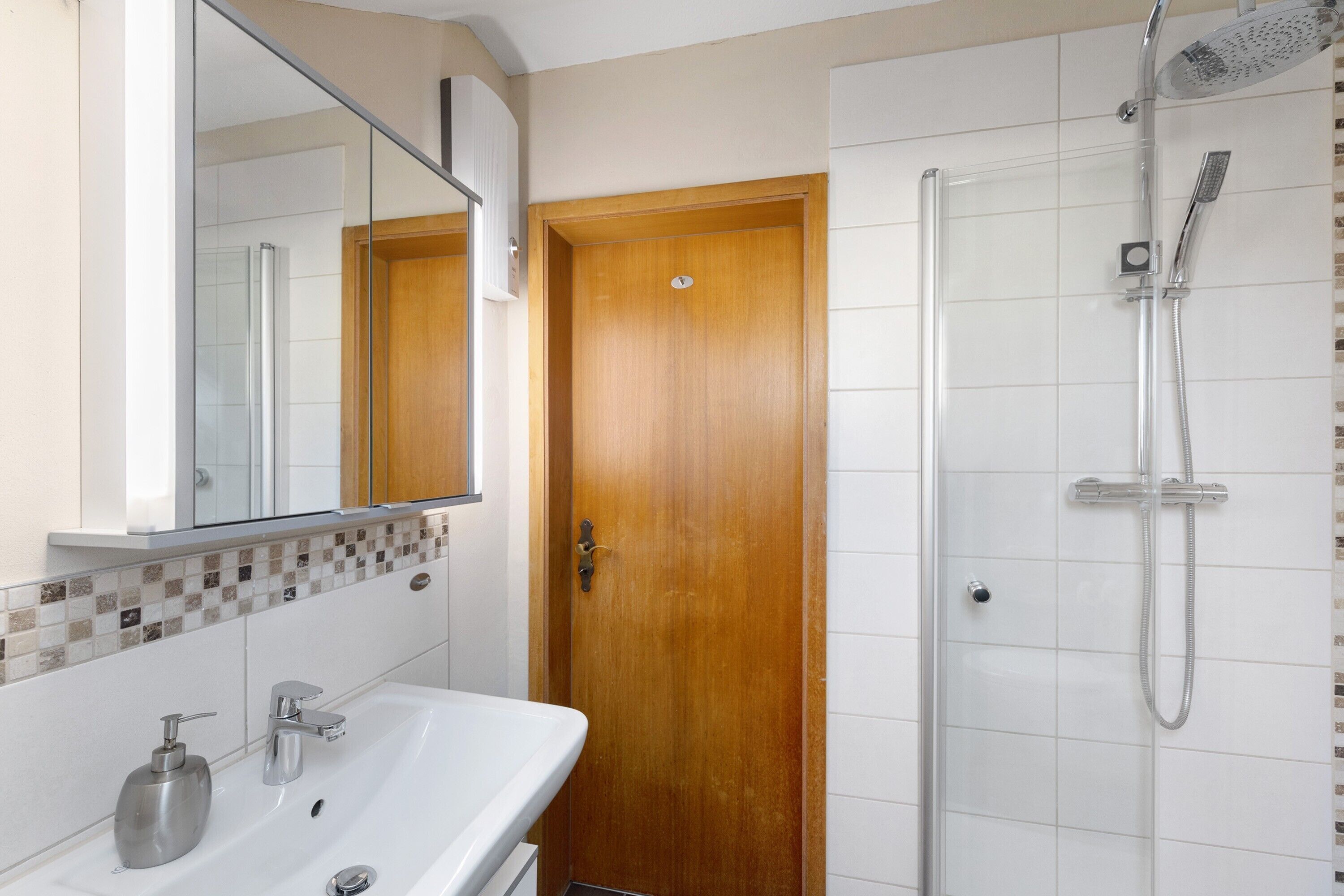 Un baño con lavabo, espejo, ducha y puerta de madera.