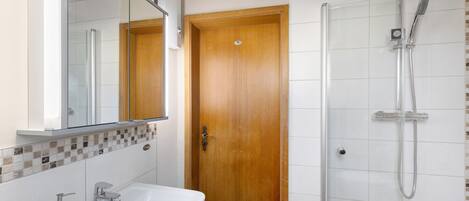 Un baño con lavabo, espejo, ducha y puerta de madera.