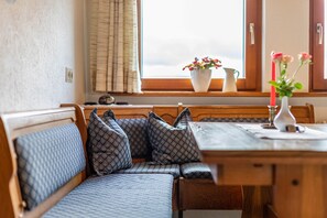 A wooden bench with patterned cushions, a table with a vase of flowers, and a window with curtains. - Apartment 'Ferienwohnung Morgensonne' with Mountain View, Shared Garden and Wi-Fi (Breitnau)