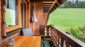 Una terraza de madera con una mesa, sillas, un farol y vistas a un campo verde.