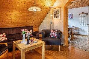 Ein gemütliches Zimmer mit Holzboden, einer Couch, einem Sessel, einem Tisch mit Blumenvase und einem Essbereich.