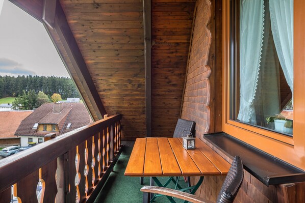 A wooden balcony with a table and chairs, a view of houses, and a window with curtains. - Apartment 'Ferienwohnung Morgensonne' with Mountain View, Shared Garden and Wi-Fi (Breitnau)