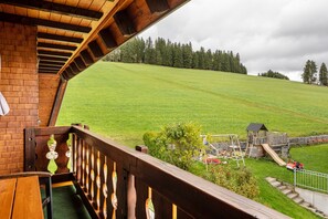 Varanda de madeira com vista para um parquinho e um campo gramado.