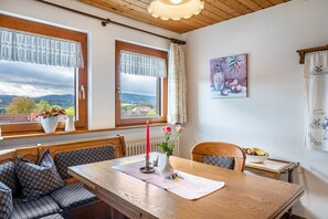 Uma sala de jantar com mesa de madeira, bancos, um vaso com flores e um quadro na parede.