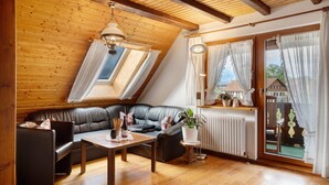 A cozy room with a wooden ceiling, a black leather sofa, a wooden table, and a window with curtains. - Apartment 'Ferienwohnung Abendrot' with Mountain View, Shared Garden and Wi-Fi (Breitnau)