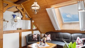 A cozy room with a wooden ceiling, a black leather sofa, a wooden table with a bottle and glasses, and a large window with curtains. - Apartment 'Ferienwohnung Abendrot' with Mountain View, Shared Garden and Wi-Fi (Breitnau)