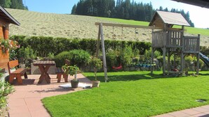 A wooden playhouse with a slide, a picnic table with benches, and a grassy yard. - Apartment 'Ferienwohnung Abendrot' with Mountain View, Shared Garden and Wi-Fi (Breitnau)